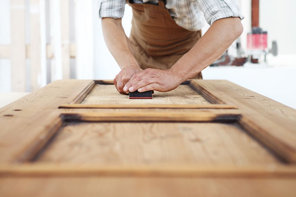 Ein Mann schleift Holz an einem Tisch, um eine glatte Oberfläche zu erzielen.